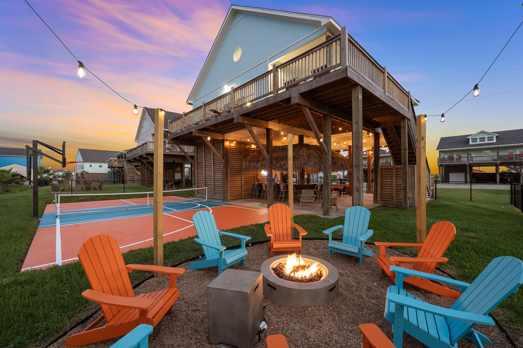 Pickle Beach vacation rental at twilight with fire pit, pickleball court, and string lights
